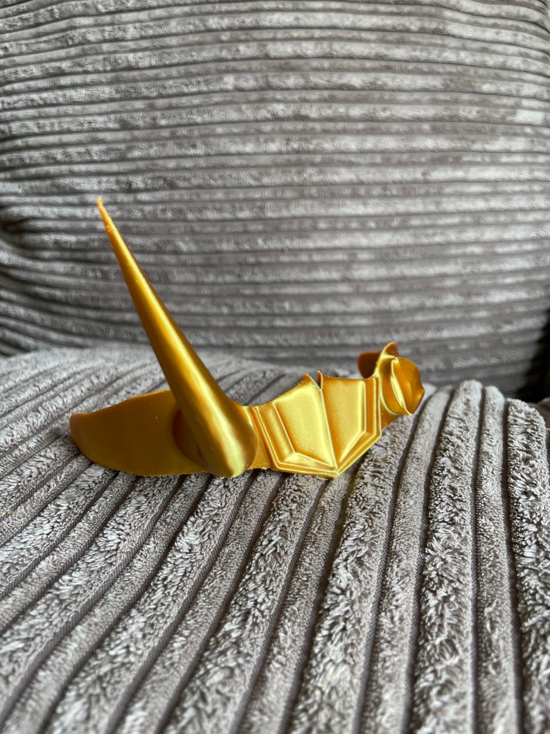 May include: A gold-colored crown with a pointed tip, resting on a gray textured surface.