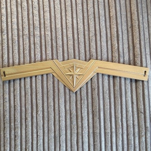 May include: A gold-coloured plastic headband with a star-shaped design in the centre. The headband is shaped like a crown.