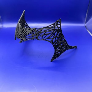 May include: A black headpiece with a web-like, open design. The headpiece has a pointed, angular shape. The object is set against a solid blue background. The intricate pattern gives it a delicate yet striking appearance.