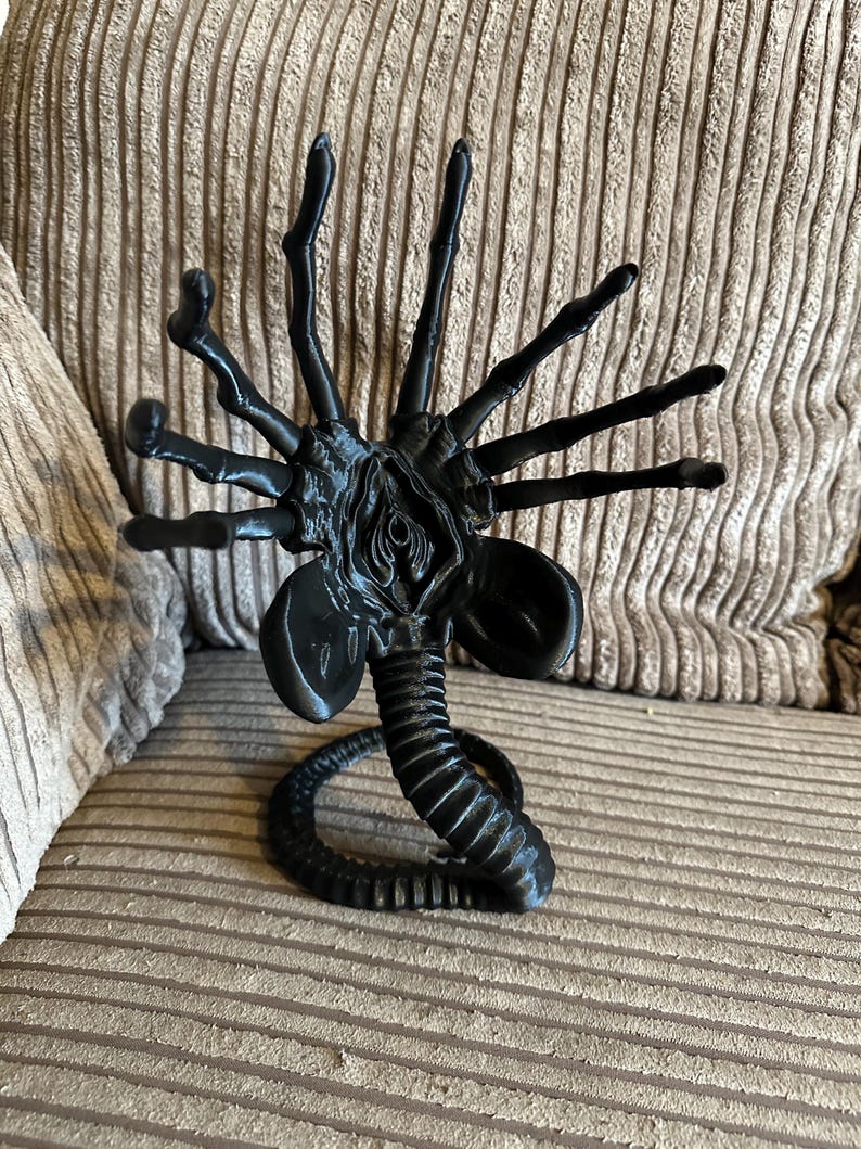Op de afbeelding: Zwarte plastic figuur van een buitenaards wezen met meerdere poten en een lange staart. Het wezen heeft een gedetailleerd, gesegmenteerd lichaam en een grote, open mond.