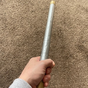 K&ouml;nnte beinhalten: Ein silberner Zauberstab aus Metall mit einer goldenen Spitze. Der Zauberstab ist mit Markierungen versehen.