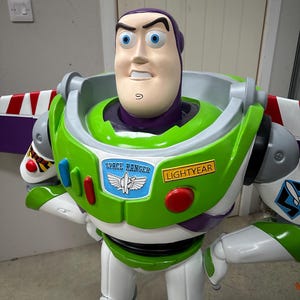 May include: A large, colorful Buzz Lightyear figure from the Toy Story franchise. The figure features a white and green spacesuit with red and blue accents, and the words "SPACE RANGER" and "LIGHTYEAR" are visible. The figure has a determined expression.
