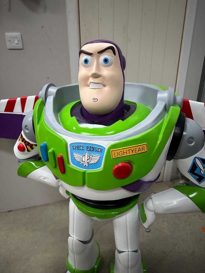 May include: A large, colorful Buzz Lightyear figure from the Toy Story franchise. The figure features a white and green spacesuit with red and blue accents, and the words "SPACE RANGER" and "LIGHTYEAR" are visible. The figure has a determined expression.