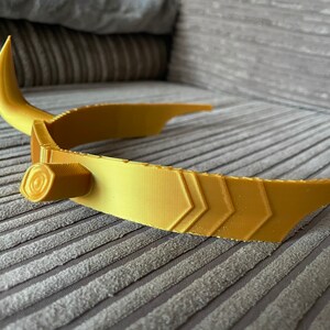 Puede incluir: Un tocado dorado con cuernos curvos y puntiagudos. El tocado presenta una superficie texturizada con dise&ntilde;os geom&eacute;tricos y un detalle cil&iacute;ndrico en el lateral. Probablemente sea un accesorio de disfraz o un objeto decorativo.