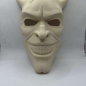 May include: A cream-colored mask with a sinister grin, prominent nose, and eye openings. The mask features two curved horns and a textured surface, evoking a menacing character. Ideal for cosplay or Halloween.