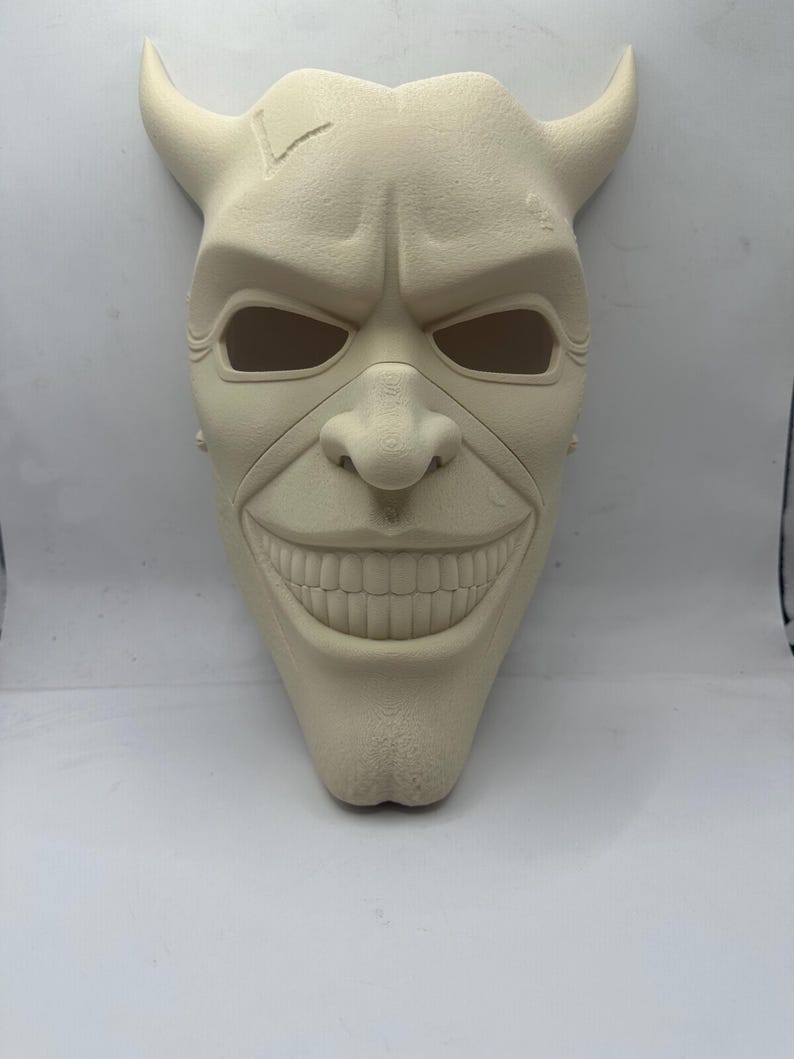 May include: A cream-colored mask with a sinister grin, prominent nose, and eye openings. The mask features two curved horns and a textured surface, evoking a menacing character. Ideal for cosplay or Halloween.