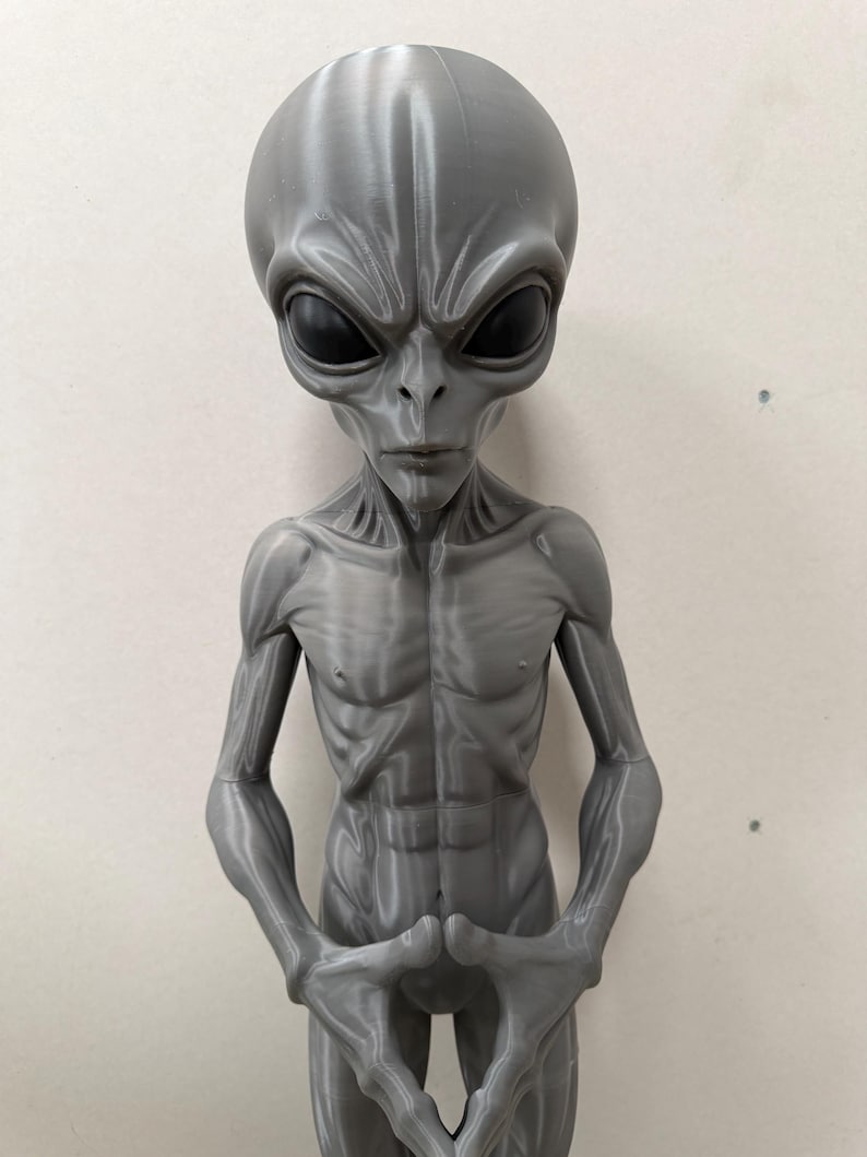 Pode incluir: Uma figura alien&iacute;gena cinza impressa em 3D com uma cabe&ccedil;a grande, lisa e alongada, com olhos pretos s&oacute;lidos em forma de am&ecirc;ndoa. A figura tem um torso esguio e musculoso com costelas e abdominais vis&iacute;veis, e bra&ccedil;os longos com as m&atilde;os juntas.