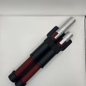 May include: A pair of black and red telescopic batons with silver accents. The batons are attached to a black holster.