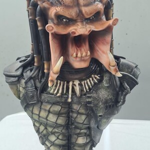 Puede incluir: Busto detallado de un alien&iacute;gena Predator, con una cabeza marr&oacute;n texturizada con rastas y una expresi&oacute;n amenazante. El busto incluye las mand&iacute;bulas, colmillos y armadura distintivos del Predator, con una base. La paleta de colores incluye tonos de marr&oacute;n, gris y negro.