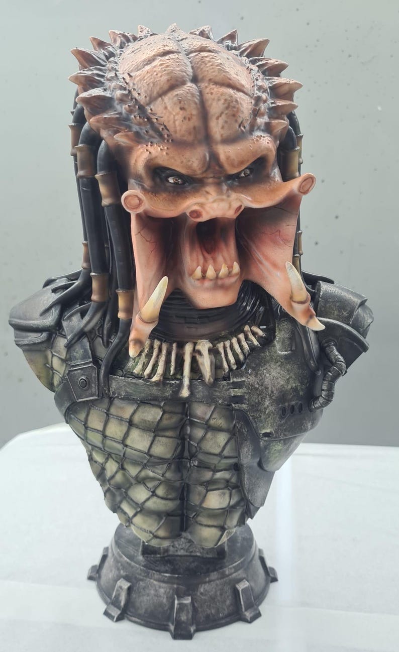 Puede incluir: Busto detallado de un alien&iacute;gena Predator, con una cabeza marr&oacute;n texturizada con rastas y una expresi&oacute;n amenazante. El busto incluye las mand&iacute;bulas, colmillos y armadura distintivos del Predator, con una base. La paleta de colores incluye tonos de marr&oacute;n, gris y negro.