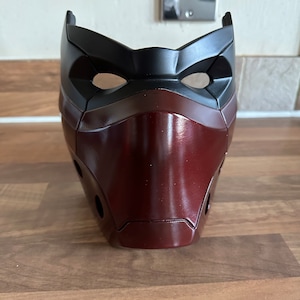 May include: A red and black plastic mask with a sleek, modern design. The mask has a raised, textured surface and two eye holes.