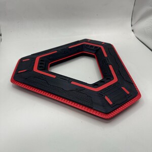 May include: A black and red geometric object with a triangular shape and a hollow centre. The object has a textured surface with red accents and a red border. The design appears to be 3D-printed.
