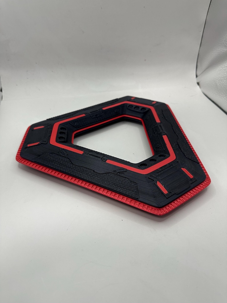 May include: A black and red geometric object with a triangular shape and a hollow centre. The object has a textured surface with red accents and a red border. The design appears to be 3D-printed.