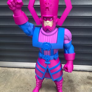 May include: A large, stylized action figure of Galactus, a comic book character. The figure is predominantly blue and magenta, with a detailed helmet and armor. The figure is posed with one fist raised, showcasing its imposing stature.