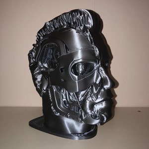 May include: A 3D printed bust of a robot head with a detailed, textured surface. The bust is black and has a futuristic design.