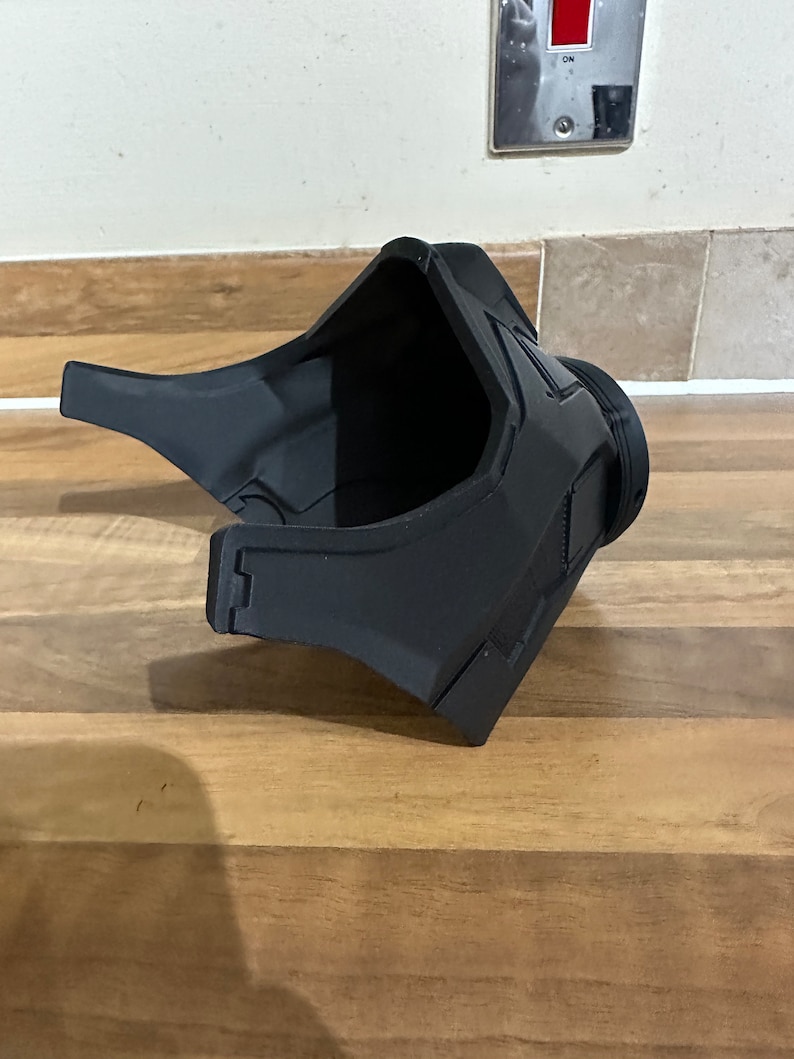May include: A black plastic 3D printed helmet with a visor. The helmet has a textured surface and a curved design.