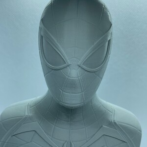 May include: A grey 3D printed bust of Spider-Man. The bust features a detailed design of Spider-Man's mask and suit.