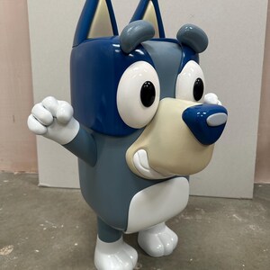 May include: A blue and white cartoon dog toy with a big smile and large eyes. The toy is made of plastic and has a blocky design.