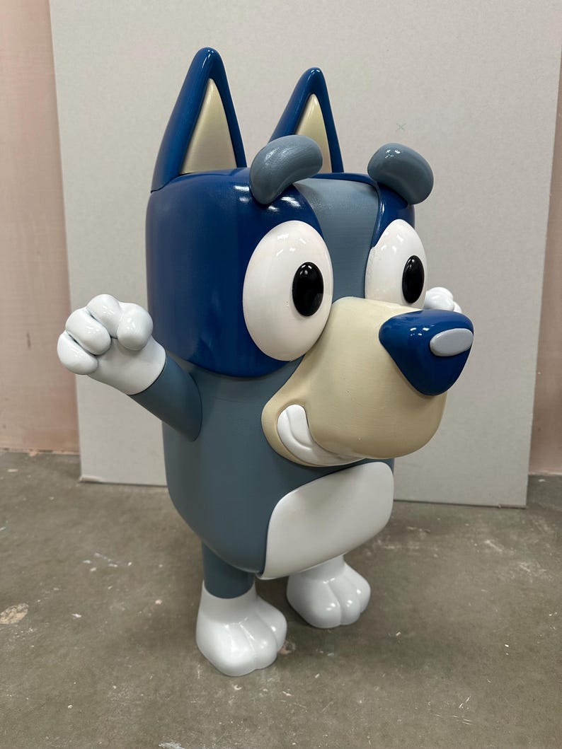 May include: A blue and white cartoon dog toy with a big smile and large eyes. The toy is made of plastic and has a blocky design.