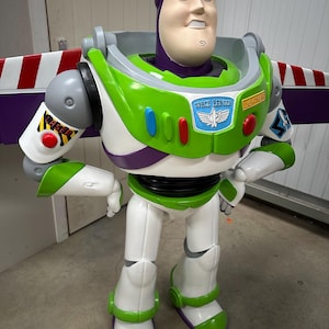 May include: A large Buzz Lightyear figure, featuring a white, green, and purple spacesuit. The figure has a light-skinned face with blue eyes and a determined expression. The chest displays a Space Ranger badge and the word "LIGHTYEAR".