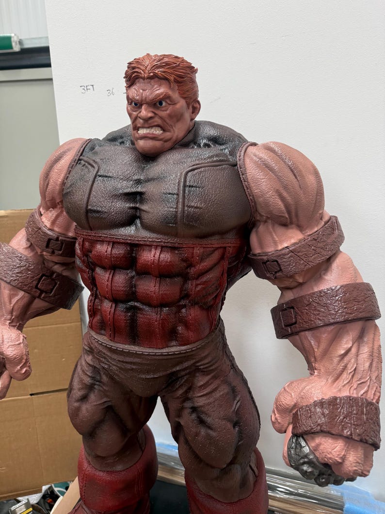 May include: A large, muscular figurine of a character with red hair and a stern expression. The figure is predominantly red and brown, with detailed musculature and armor-like elements. The figure's arms are massive, and it has a determined facial expression.