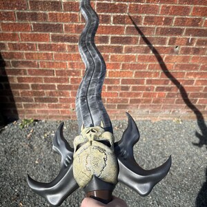 May include: A fantasy sword with a curved, silver blade and a skull-shaped hilt. The hilt is tan and brown, with two curved, black wings extending from the sides. The sword has a long, wavy blade.