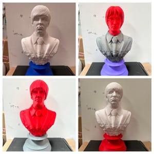 May include: A collection of four busts of a man with a distinctive hairstyle and suit. The busts are in various colors: white, red, and gray. Each bust is mounted on a colored base, with options including blue, purple, and red. The busts appear to be made of a solid material.