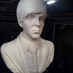 May include: A white bust sculpture of a man with short, styled hair, wearing a suit jacket, collared shirt, and tie. The sculpture is a detailed representation of a person's upper body and head.