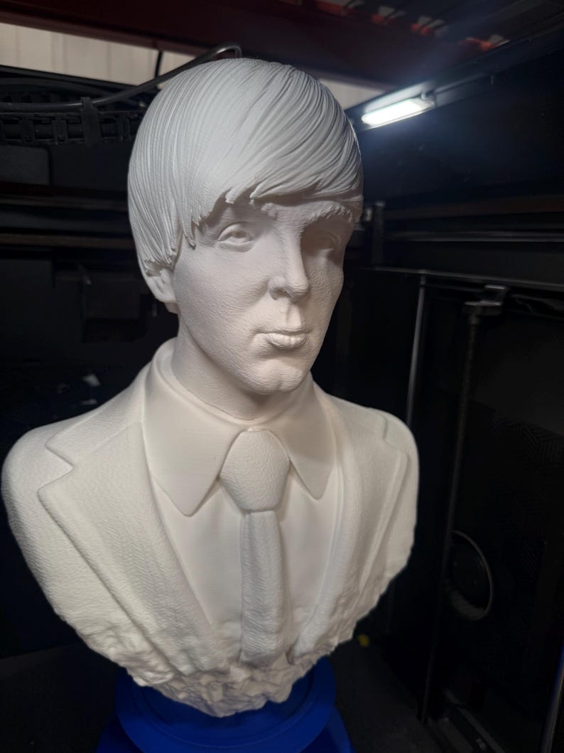 May include: A white bust sculpture of a man with short, styled hair, wearing a suit jacket, collared shirt, and tie. The sculpture is a detailed representation of a person's upper body and head.