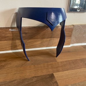 Può includere: Un cerchietto in plastica blu scuro con un design a punta nella parte anteriore. Il cerchietto è progettato per essere indossato sulla testa.