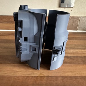 May include: A grey 3D printed object with a detailed design, split into two sections. The object has a knob and a small square opening.