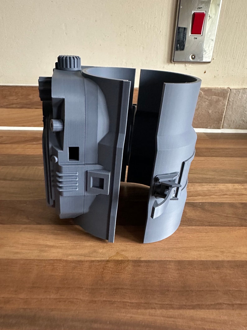 May include: A grey 3D printed object with a detailed design, split into two sections. The object has a knob and a small square opening.