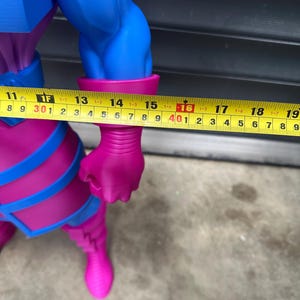 May include: A large, detailed figurine of a comic book character, predominantly blue and magenta. The figure's arm measures approximately 16 inches. The figure has a muscular build and is wearing a costume with blue accents.