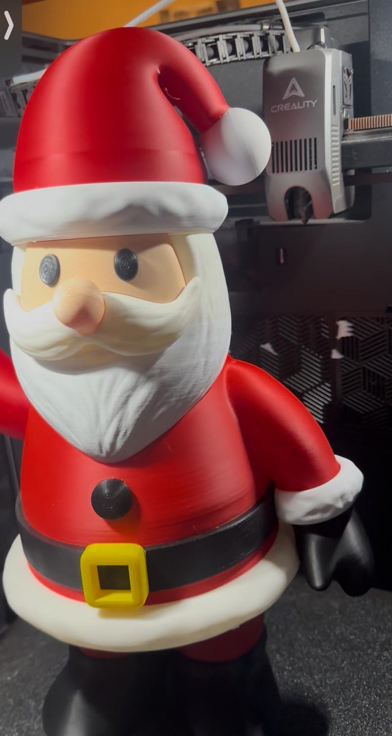 May include: A 3D-printed Santa Claus figure. The figure is predominantly red with white trim on the hat and beard. It has a black belt with a yellow buckle. The figure is a festive decoration.