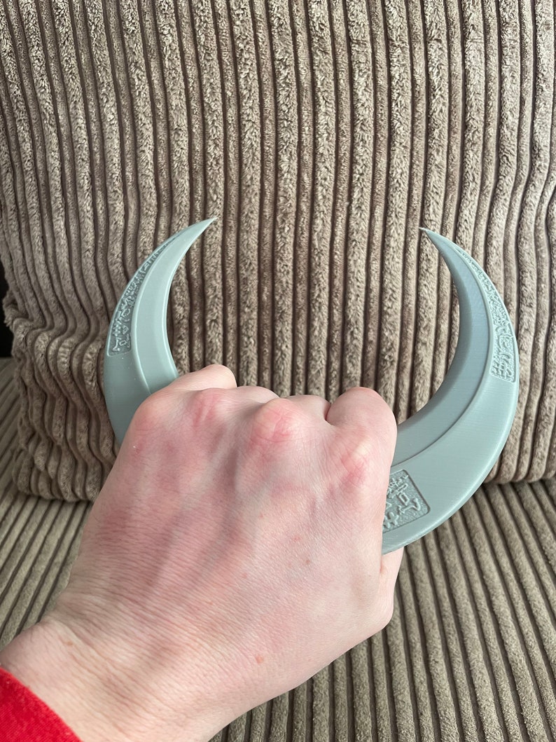 May include: A pair of gray crescent-shaped hand grippers with the text "Grip Strength" printed on them.