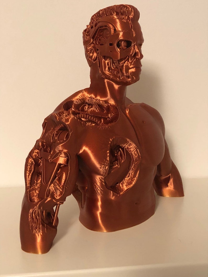 May include: A 3D printed bust of a robot with a detailed, exposed skeletal structure. The bust is made of a copper-colored material and is posed with the head turned to the side.