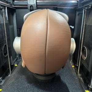 May include: A brown, spherical object is being 3D printed inside a black and silver machine. The object is split into two halves and has a textured surface. The printer bed has the word "CREALITY" printed on it.