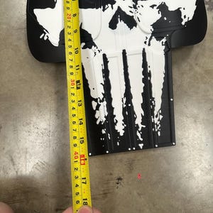 May include: Black and white skull-shaped object, approximately 18 inches long, with a distressed paint effect. The design features a skull with a prominent nose and teeth. The object is likely a decorative item or prop.
