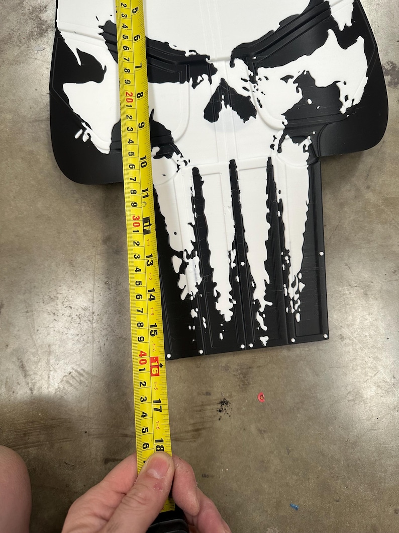 May include: Black and white skull-shaped object, approximately 18 inches long, with a distressed paint effect. The design features a skull with a prominent nose and teeth. The object is likely a decorative item or prop.