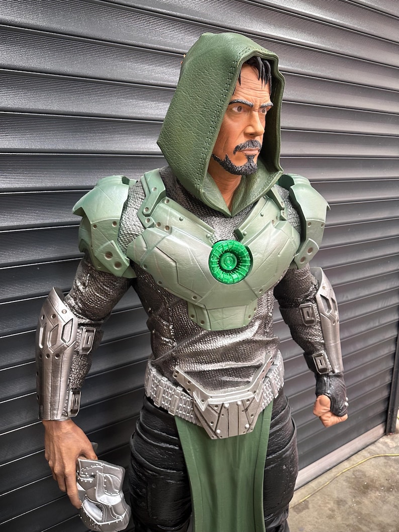 May include: A detailed statue of a character in a green hooded cloak and armor. The figure has a stern expression and a goatee. The armor is a mix of silver and green, with a glowing green chest piece. The figure is holding a silver gauntlet.
