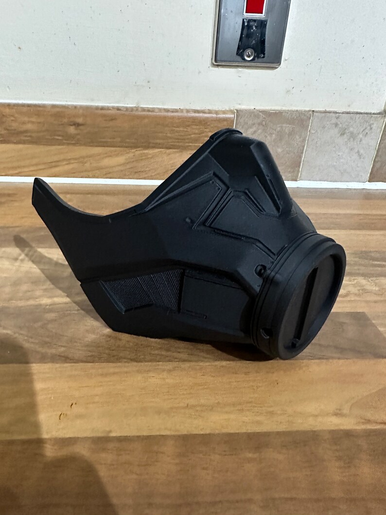 May include: A black plastic mask with a futuristic design. The mask has a large, round opening on the right side.