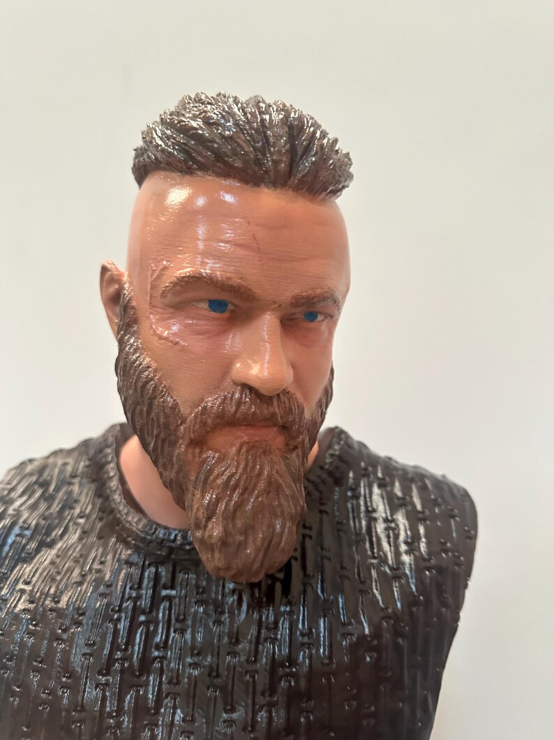 May include: A bust of a man with a brown beard and hair, and blue eyes. The figure has a scar on the face and is wearing a dark textured shirt. The bust is a detailed representation of a historical or fictional character.