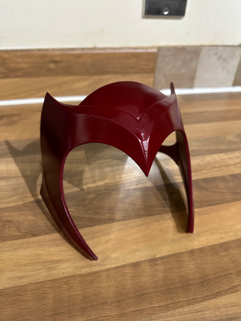May include: A red plastic headband with a pointed, curved design. The headband is made to look like a crown.