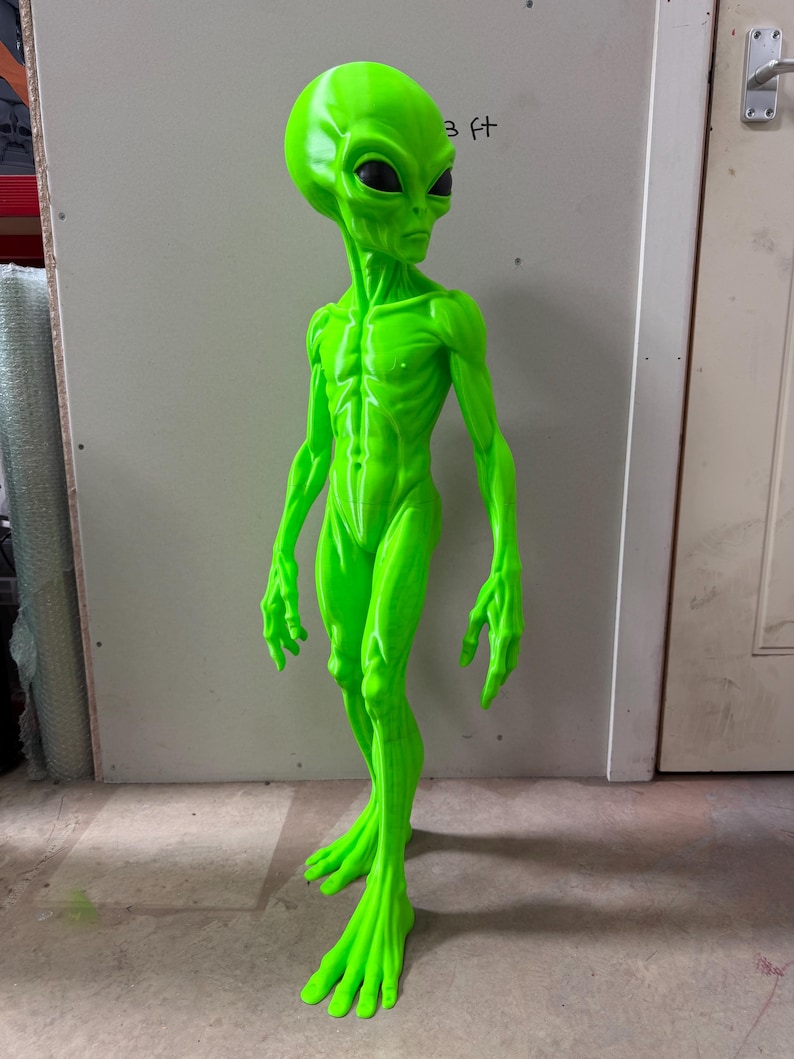 Pode incluir: Uma figura alien&iacute;gena verde n&eacute;on brilhante com uma cabe&ccedil;a alongada, grandes olhos pretos em forma de am&ecirc;ndoa e um corpo esguio e texturizado com musculatura definida. A figura est&aacute; de p&eacute; com bra&ccedil;os longos e m&atilde;os e p&eacute;s.