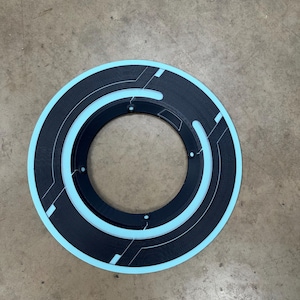 May include: A circular, black and light blue decorative object with a geometric design. The object has a ring shape with a light blue outer edge and inner ring. The design includes straight lines and small circles.