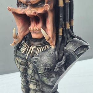 Puede incluir: Busto detallado de un alien&iacute;gena Predator, con una cabeza marr&oacute;n anaranjada texturizada, rastas y una boca abierta. El busto incluye una pieza de pecho detallada y una base, mostrando la apariencia amenazante de la criatura.