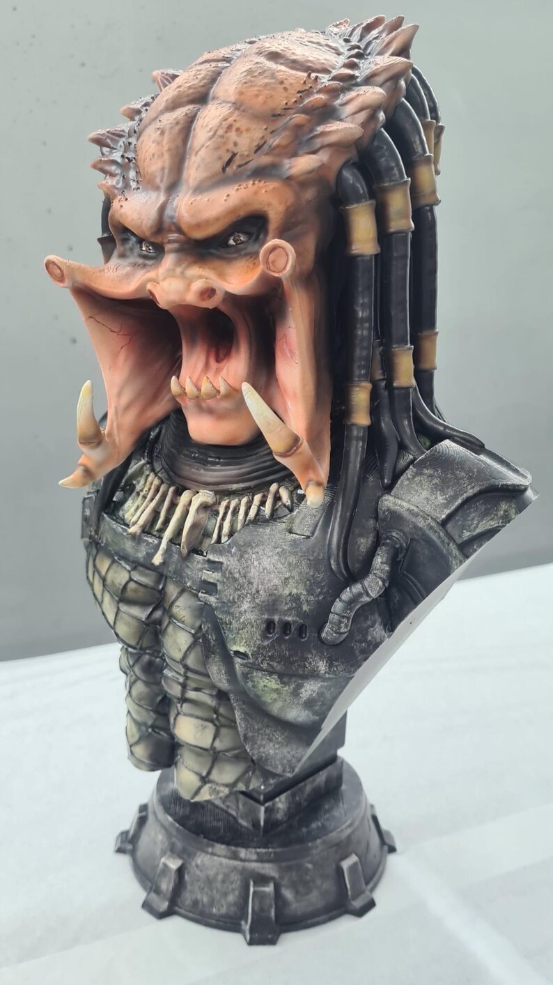 Puede incluir: Busto detallado de un alien&iacute;gena Predator, con una cabeza marr&oacute;n anaranjada texturizada, rastas y una boca abierta. El busto incluye una pieza de pecho detallada y una base, mostrando la apariencia amenazante de la criatura.