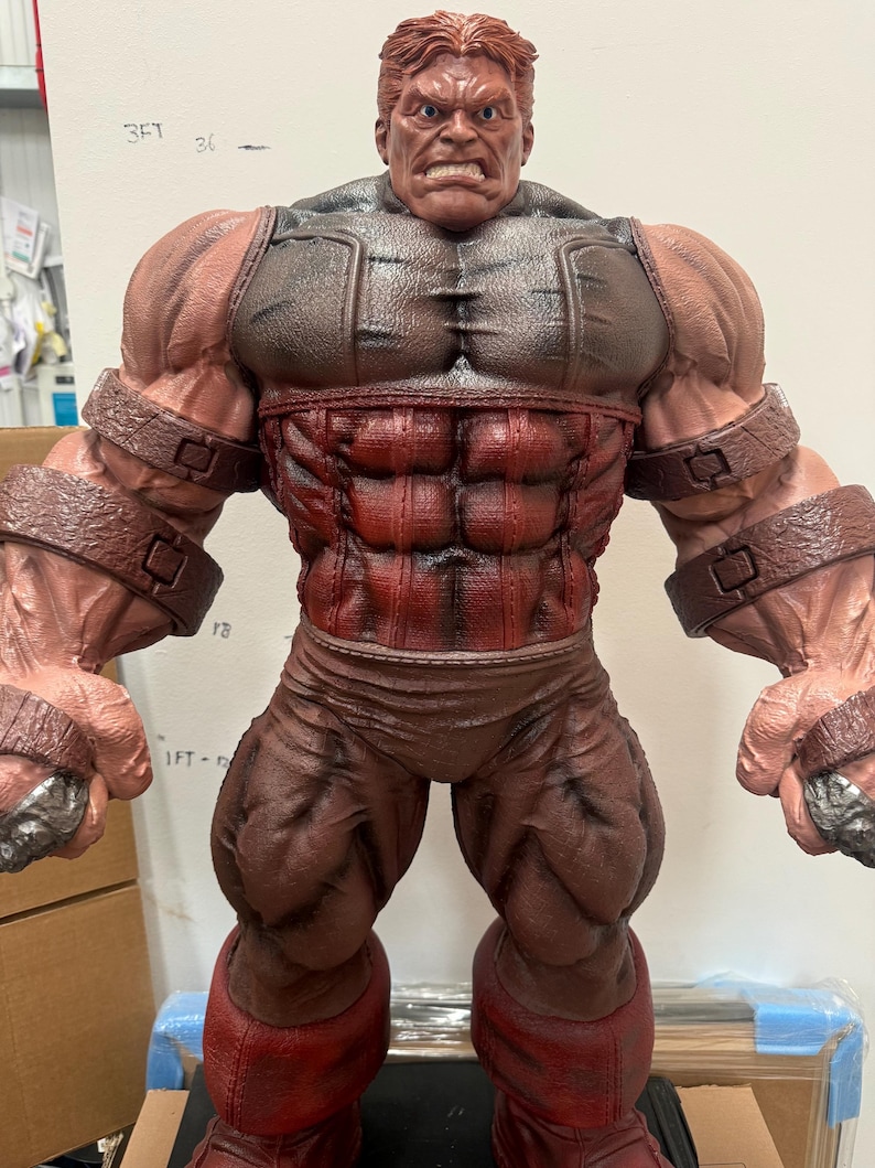 May include: A detailed figurine of a muscular character, predominantly red and brown. The figure has a stern expression, with a detailed face and hair. The costume includes a chest piece, pants, and arm bands. The figure is standing upright.