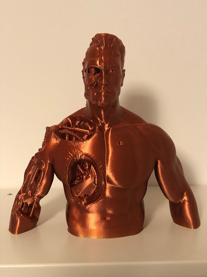 May include: A 3D printed bust of a cyborg, with one side of the face showing the exposed mechanical parts. The bust is made of a copper-colored plastic and is a detailed representation of a popular science fiction character.