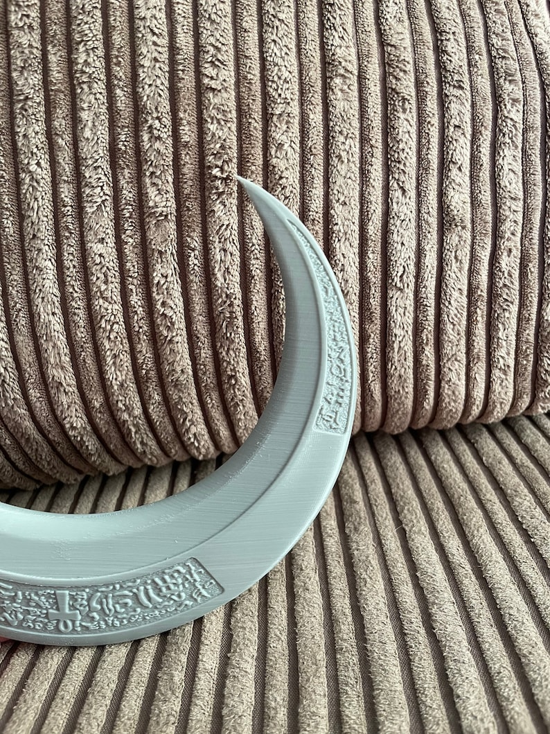 May include: A gray crescent moon-shaped object with a raised design and text around the edge. The object is made of a smooth, plastic-like material.